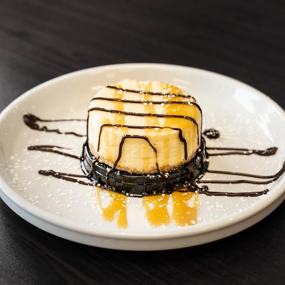 Golden dessert drizzled with chocolate and caramel, dusted with powdered sugar, and served on a white plate.