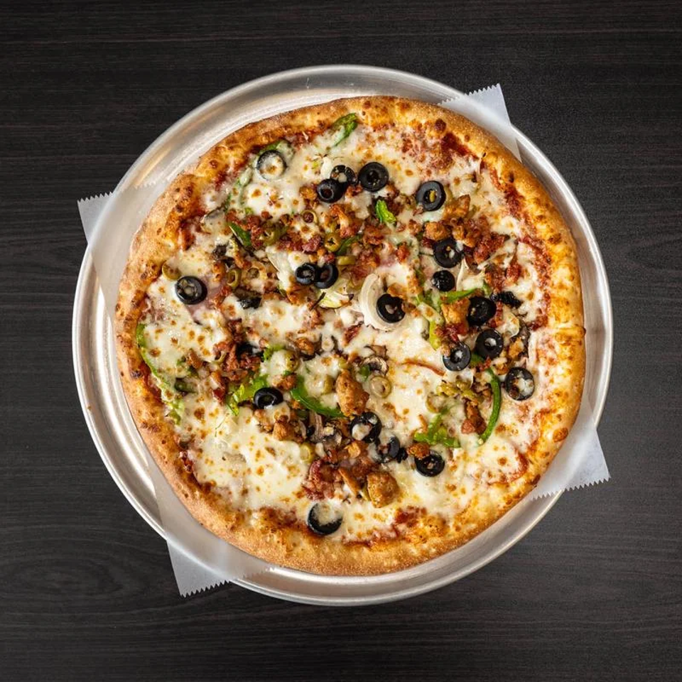 Cheesy pizza topped with black olives, mushrooms, green peppers, onions, and seasoned meat on a round metal tray.