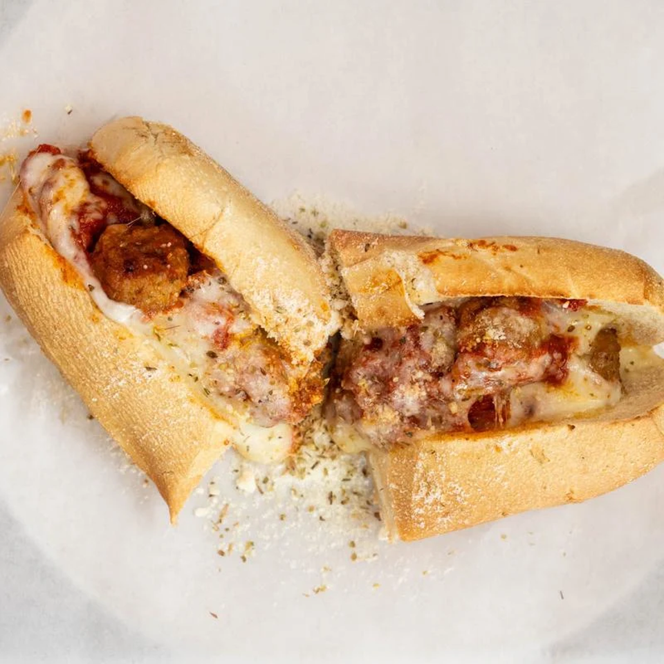 Two toasted meatball subs with melted cheese and marinara sauce on a white plate.